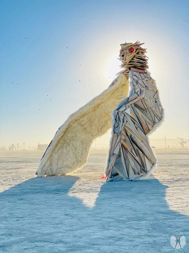 A large owl-like sculpture with red eyes placed outside in the desert.