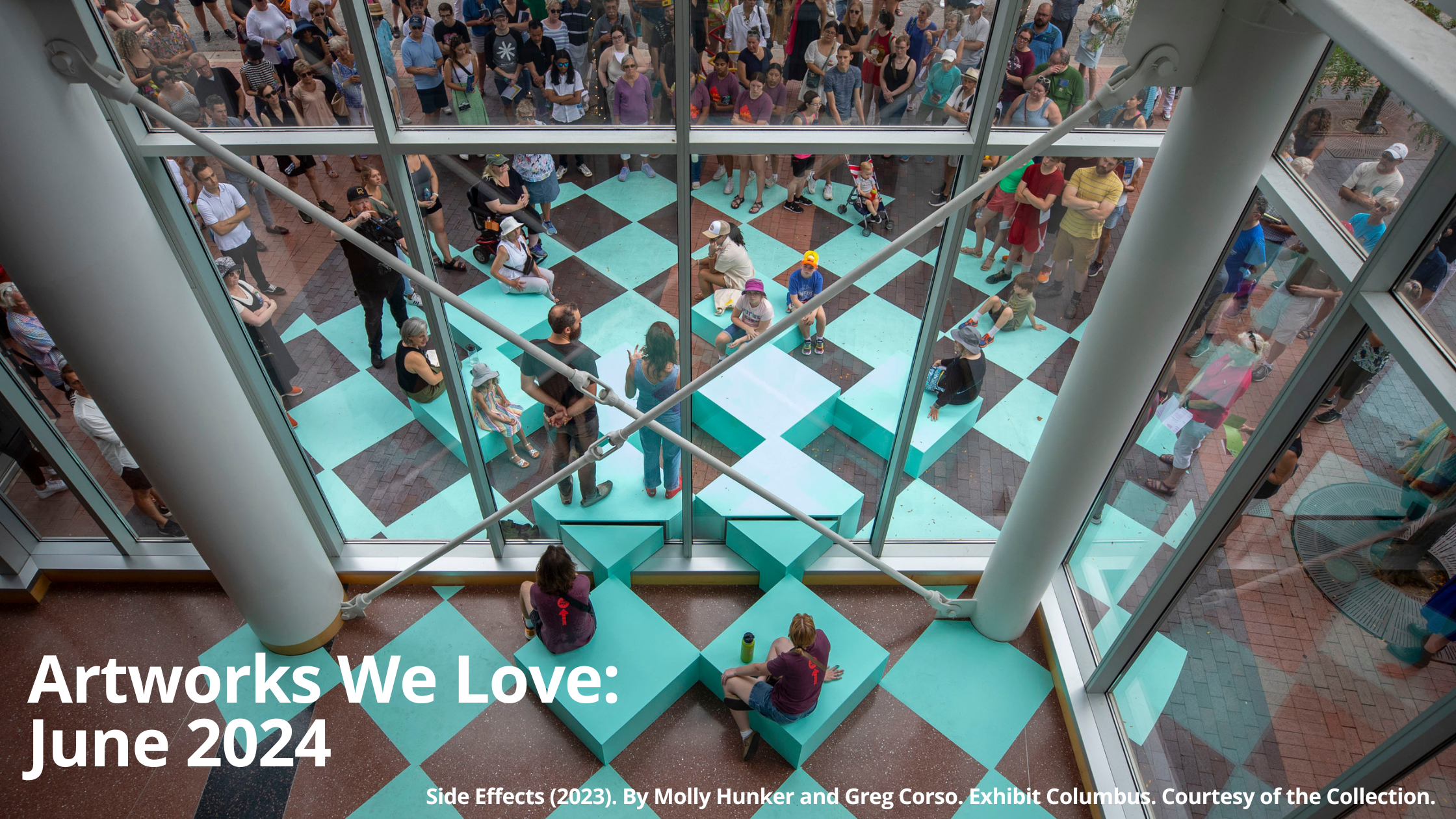 A view from above looking down onto an outdoor art installation. The installation is a series of teal-colored square blocks arranged in a checkerboard pattern. People are sitting on the blocks, interacting with the art piece. There are also many people standing behind a glass window looking down at the installation. The text "Artworks We Love: June 2024" is displayed in white letters on a blue and brown background. Below the text, it reads "Side Effects (2023). By Molly Hunker and Greg Corso. Exhibit Columbus. Courtesy of the Collection."