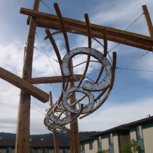 Horseshoe like sculptures hang from a large wooden frame outside of a building