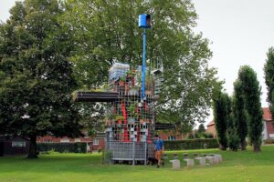 A unique metal grid structure with plants, a slide, and a water tank in a park.